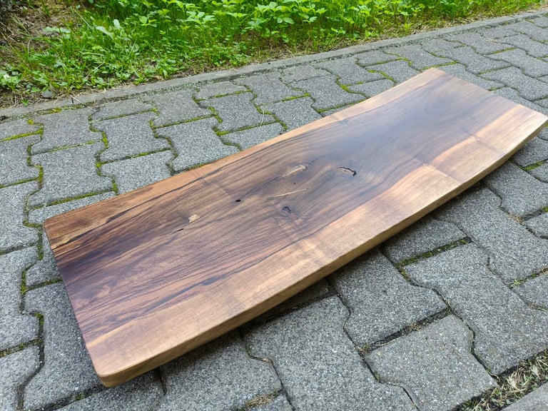 Live edge wood slab with natural grain resting on patterned pavement next to green grass