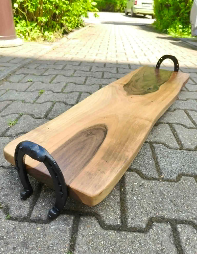 Wooden sled with black metal handles on a paved driveway with green bushes