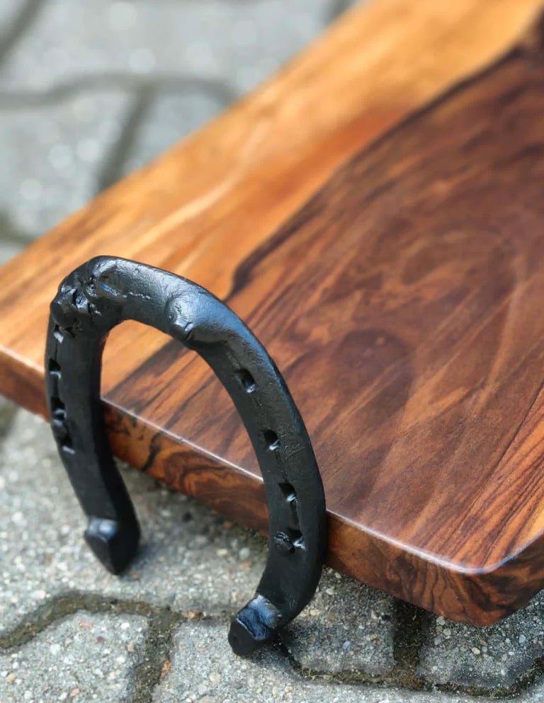 Black horseshoe leaning against wooden cutting board on concrete surface